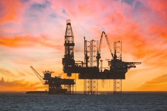 Offshore oil rig silhouetted against an orange sunset sky